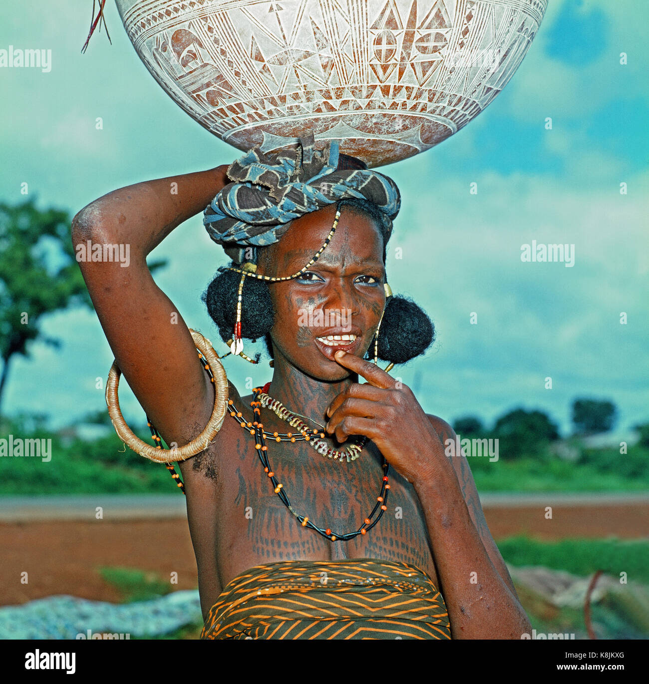 Fulani Milk Maid. Calabash, with hand incised decoration, balanced on her on head. Note facial and upper body scarifications markings as decoration. C Stock Photo