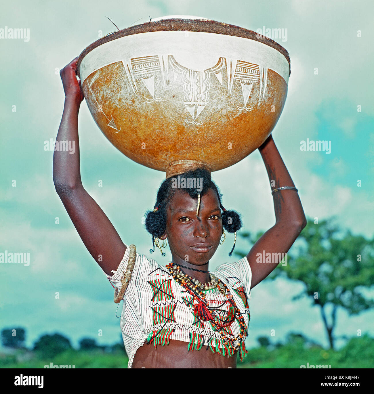 Fulani Milk Maid. Calabash, with hand incised decoration, balanced on her on head. Note facial and upper body scarifications markings as decoration. C Stock Photo
