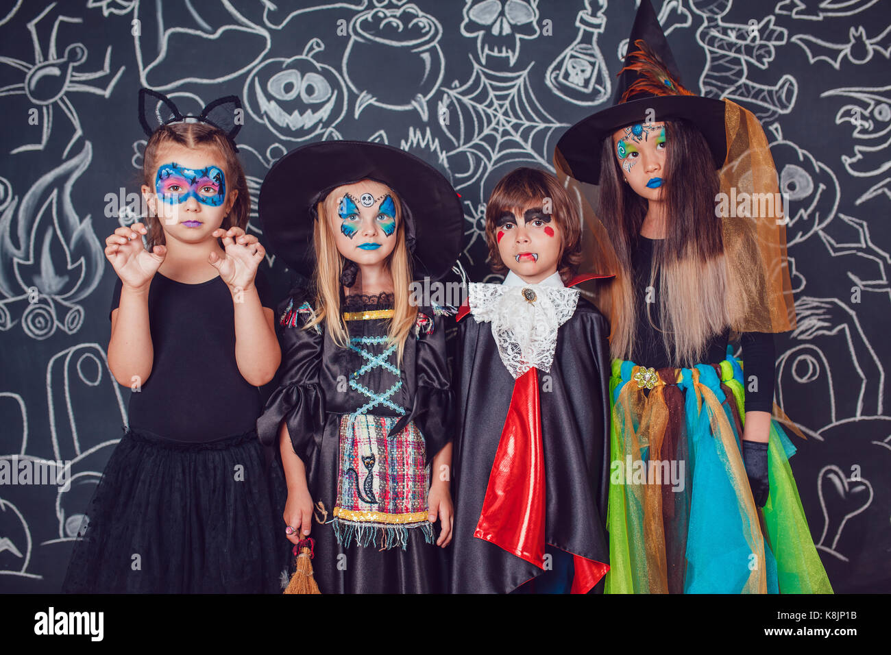 Children in scary Halloween costumes stand against a wall with drawings. Stock Photo