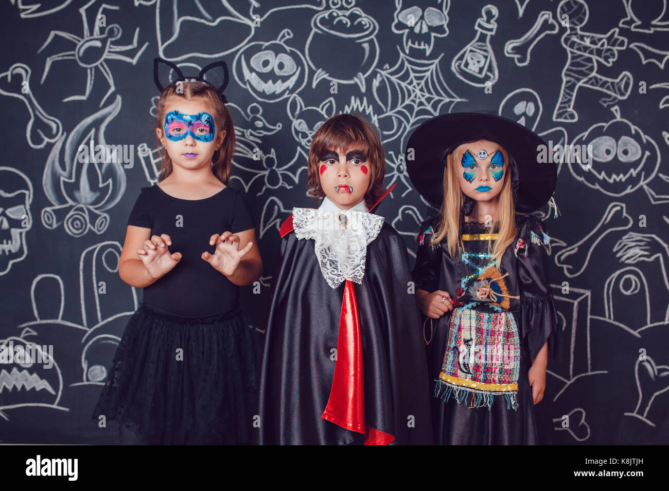 Children in scary Halloween costumes stand against a wall with drawings. Stock Photo