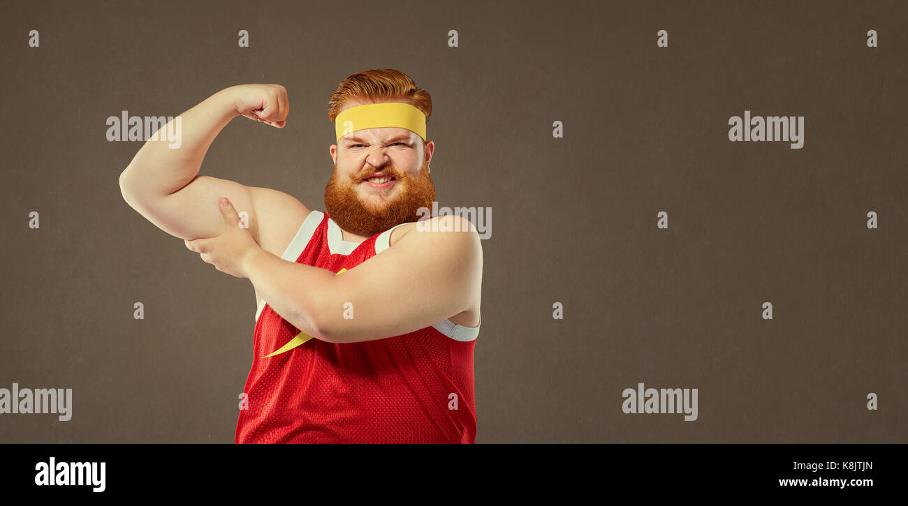 A fat man in a sport suit keeps his muscles on his arm. Stock Photo