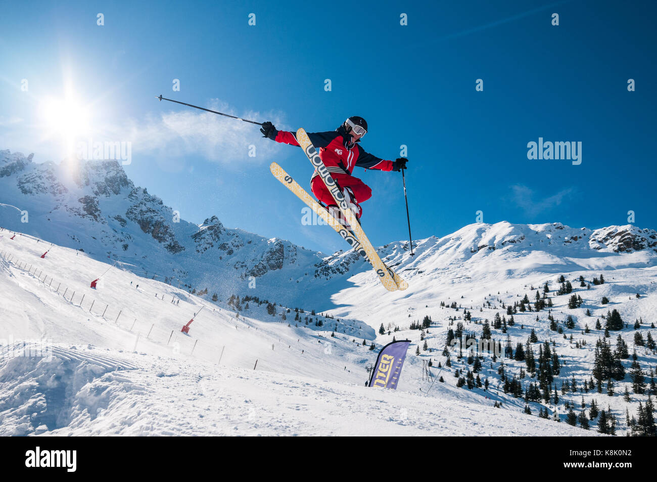 Female skier jumping off snow ramp in to the air on a sunny Winter day
