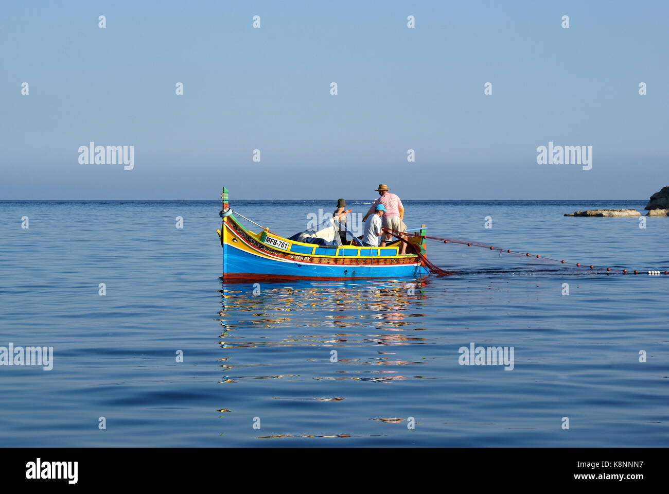 Fishing from a traditional colourful luzzu boat, Il-Hofra I-Kbira bay, Malta Stock Photo