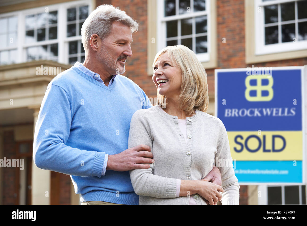 Happy Mature Couple Standing Outside House With Sold Sign Stock Photo ...