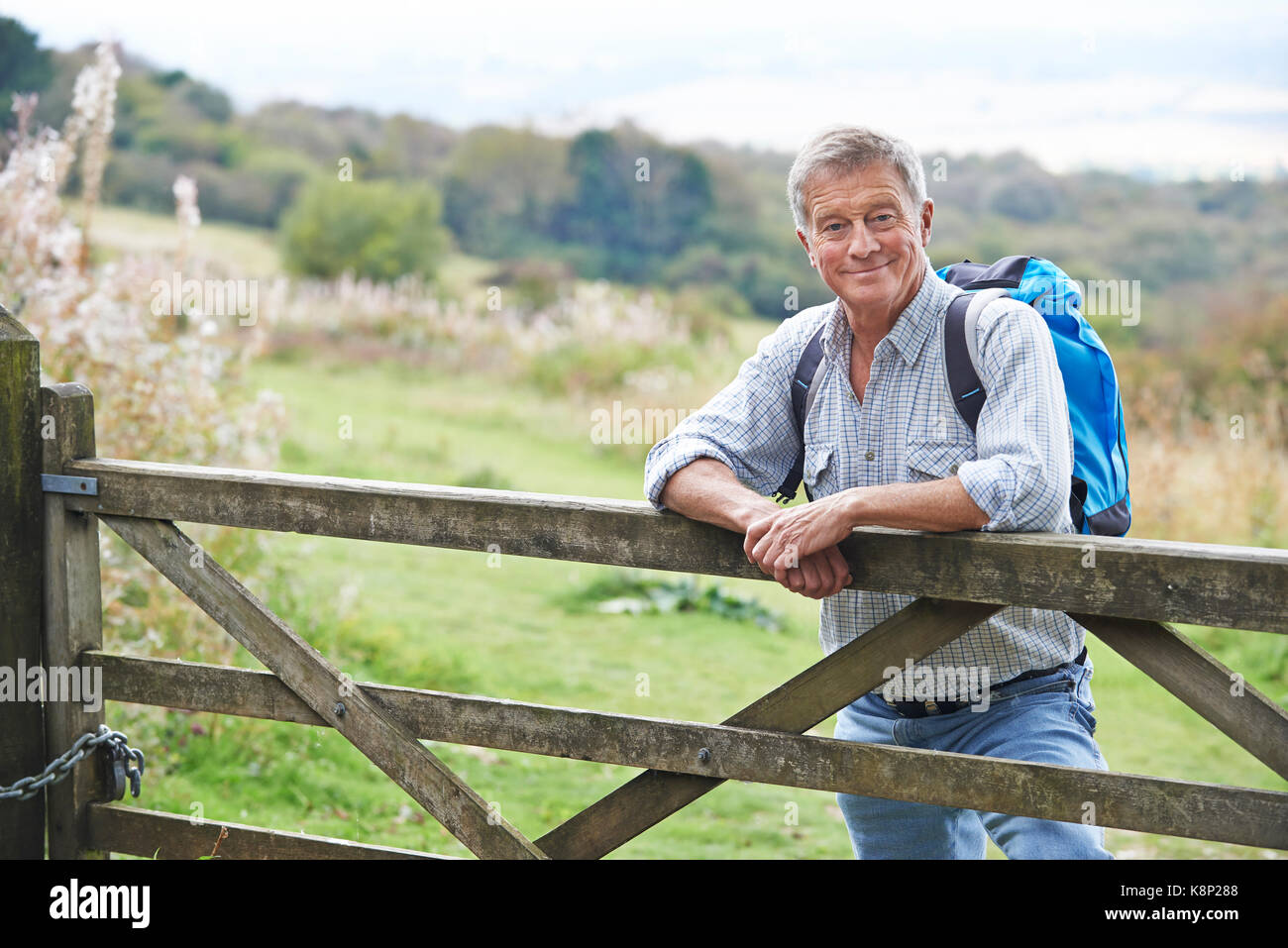 Portrait Of Senior Man On Hike In Countryside Resting By Gate Stock Photo