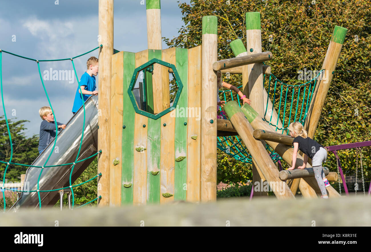 Young children playing on a wooden climbing frame in a kids playground in the UK. Stock Photo