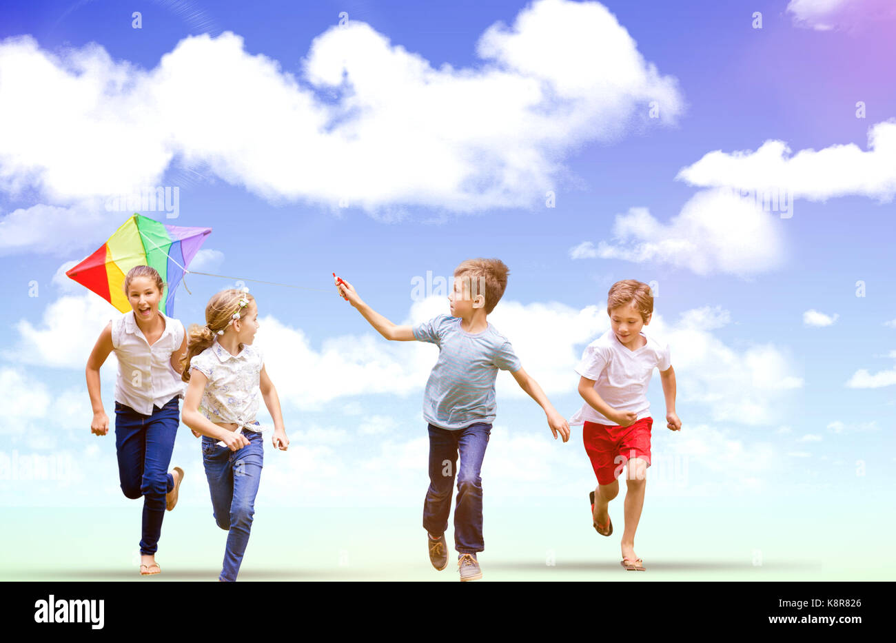Full length of boy holding kite running with friends against blue sky