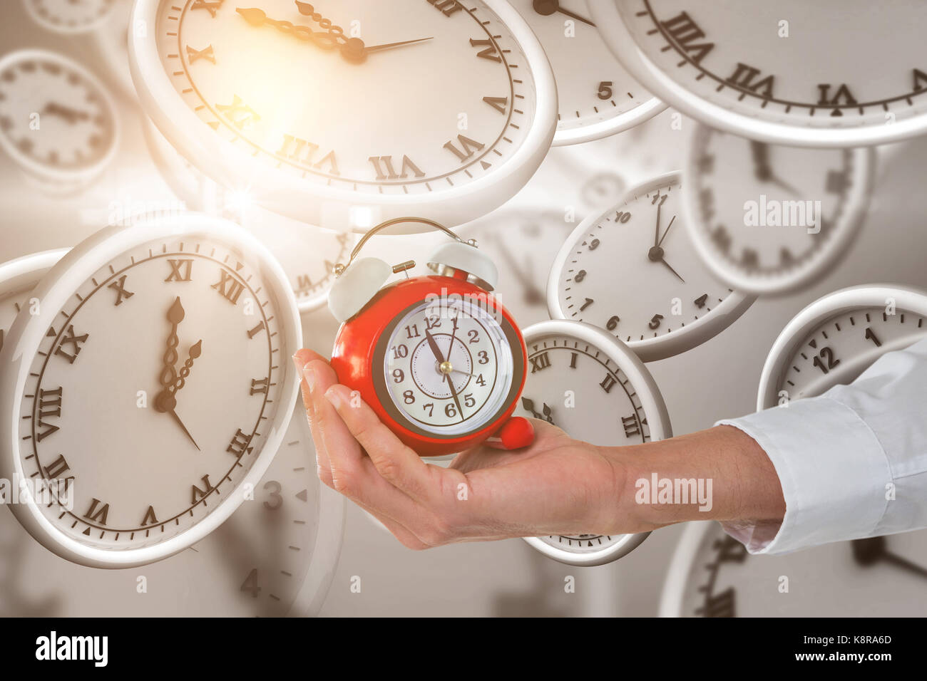 Cropped hand holding alarm clock against digitally generated image of clocks Stock Photo