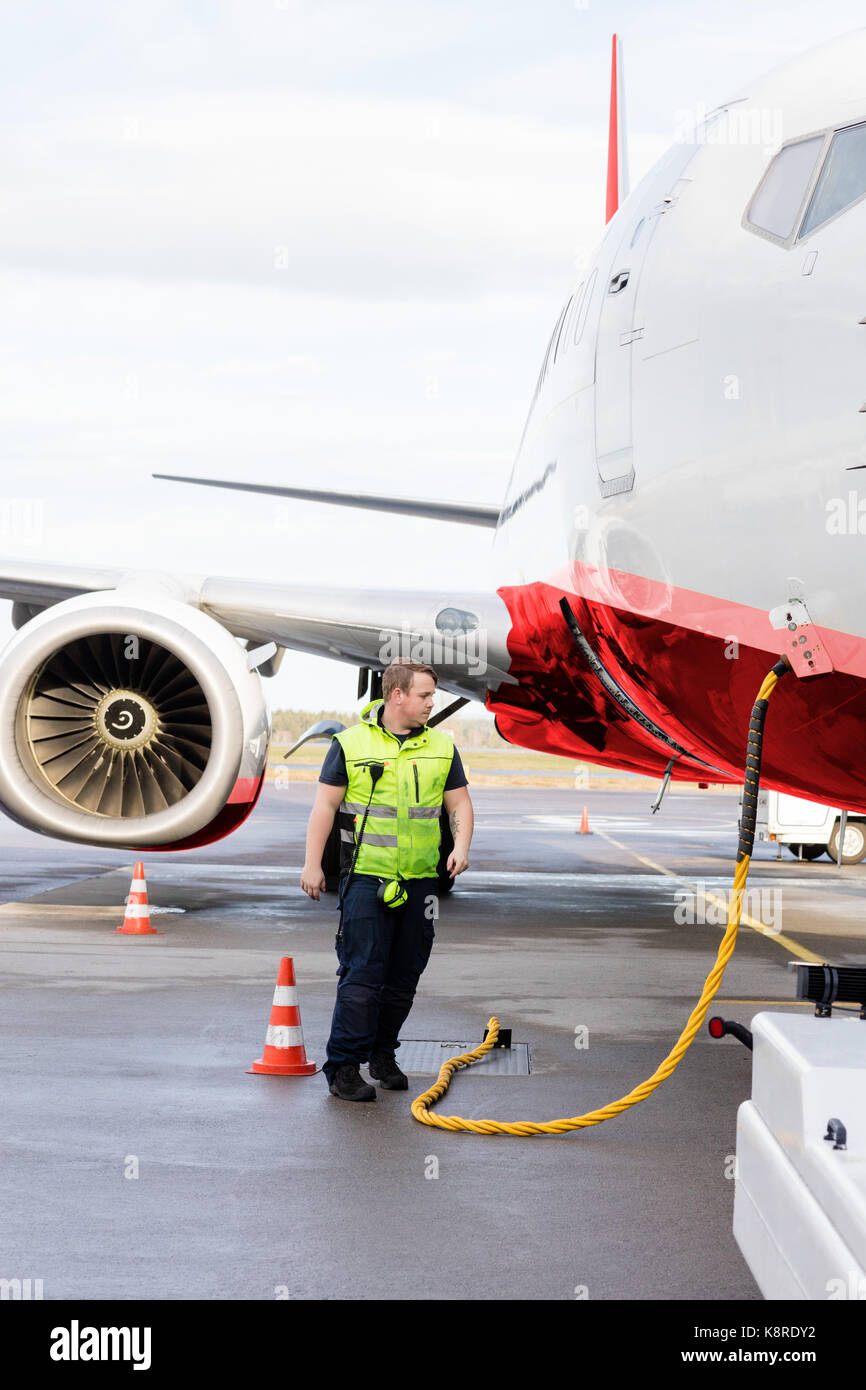 Ground Crew Member Walking By Airplane Being Charged On Runway Stock Photo