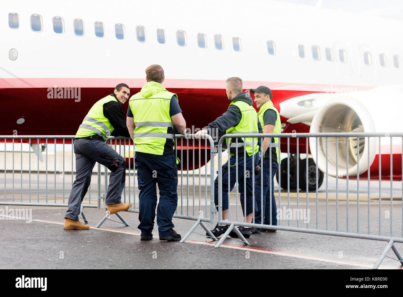Crew Communicating By Fence Against Commercial Airplane Stock Photo