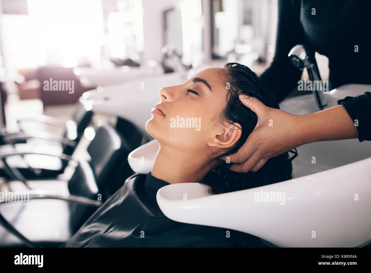 Female hairdresser rinsing hair of a customer . Woman getting hair spa treatment done at salon. Stock Photo