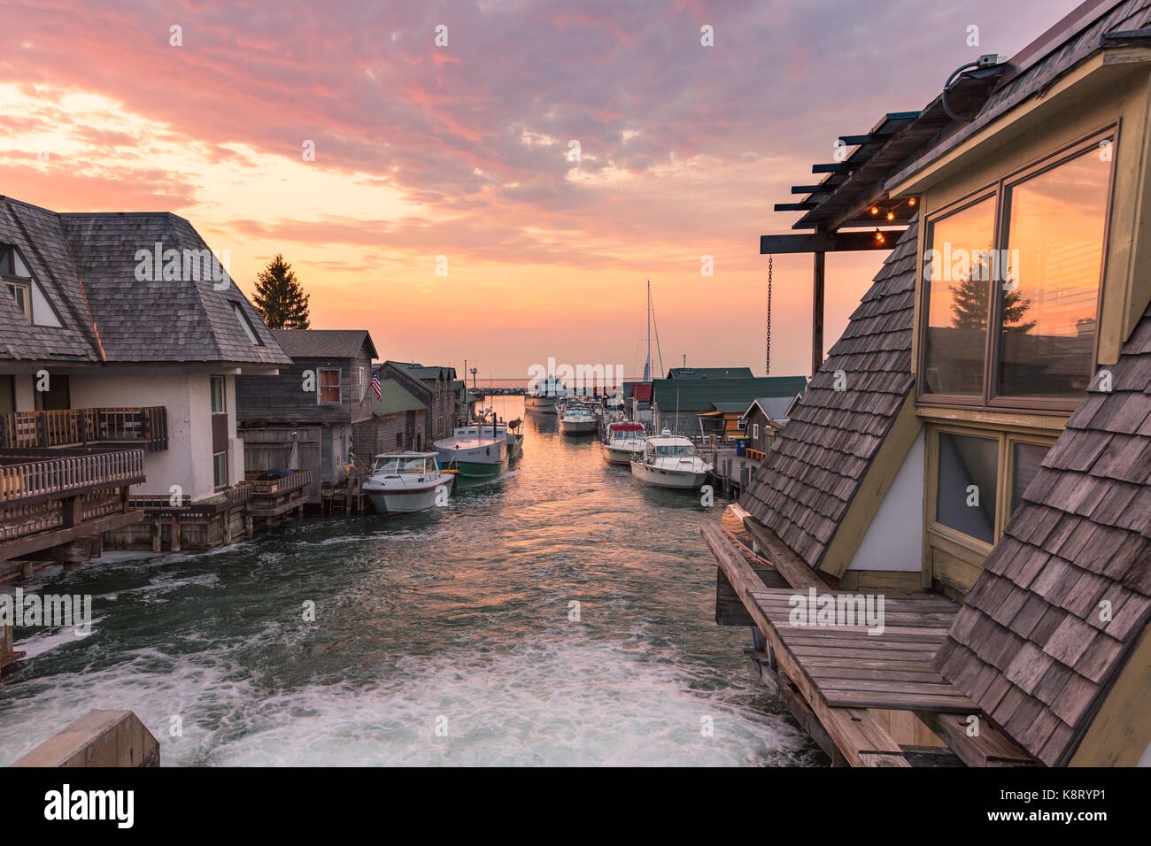 A Lake Michigan sunset illuminates Leeland Michigan, also known as Fishtown. Fishing boats line the docks and Lake Michigan is in the background Stock Photo