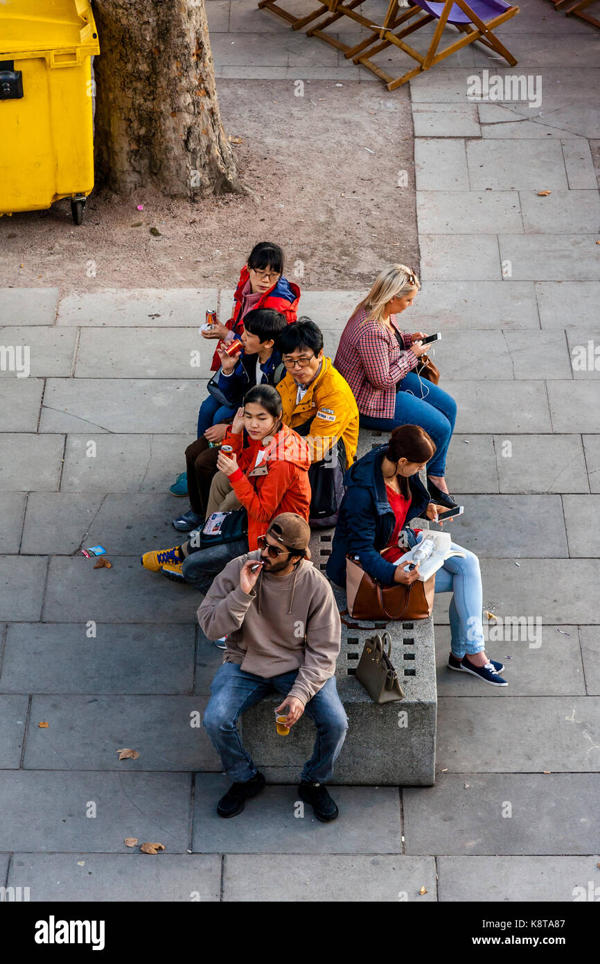 A Group Of Tourists Sitting On A Bench, The Southbank, London, UK Stock Photo