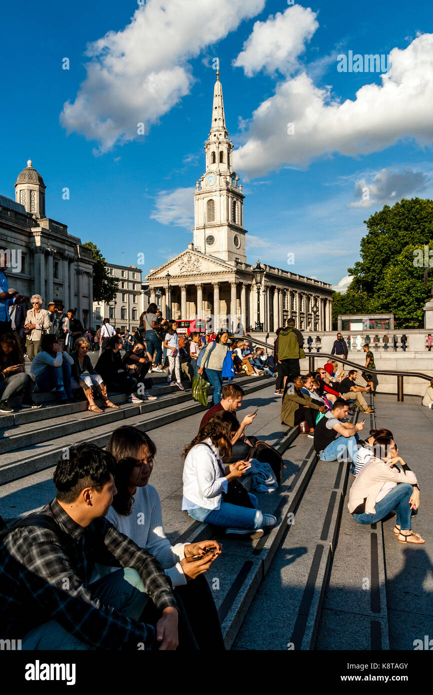 Young People Sitting On The Steps Of Trafalgar Square With The Church Of St Martin-In-The-Fields In The Backround, London, UK Stock Photo