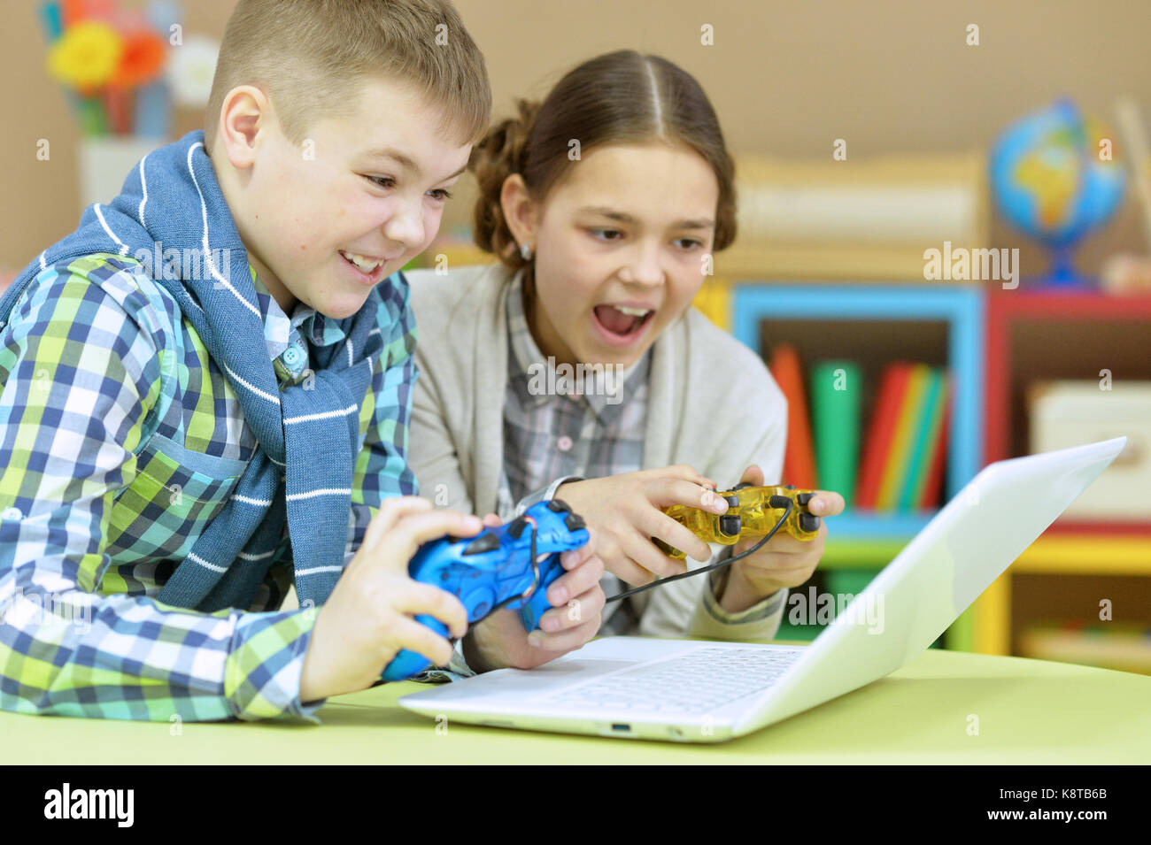 emotional brother and sister playing computer game on laptop with joysticks Stock Photo