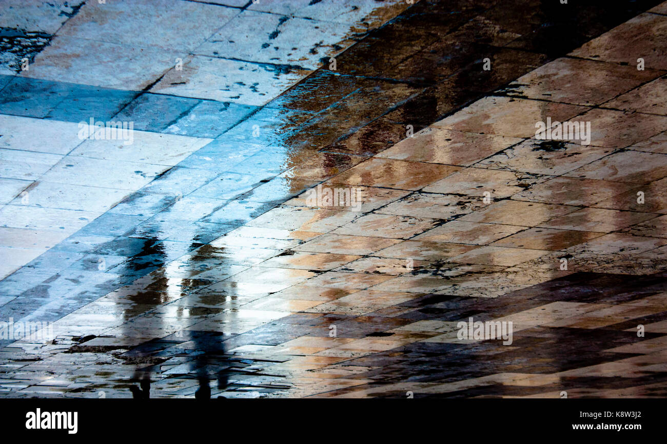 Blurry reflection shadow of a two people walking in the old ruined city pedestrian zone just after the rain Stock Photo