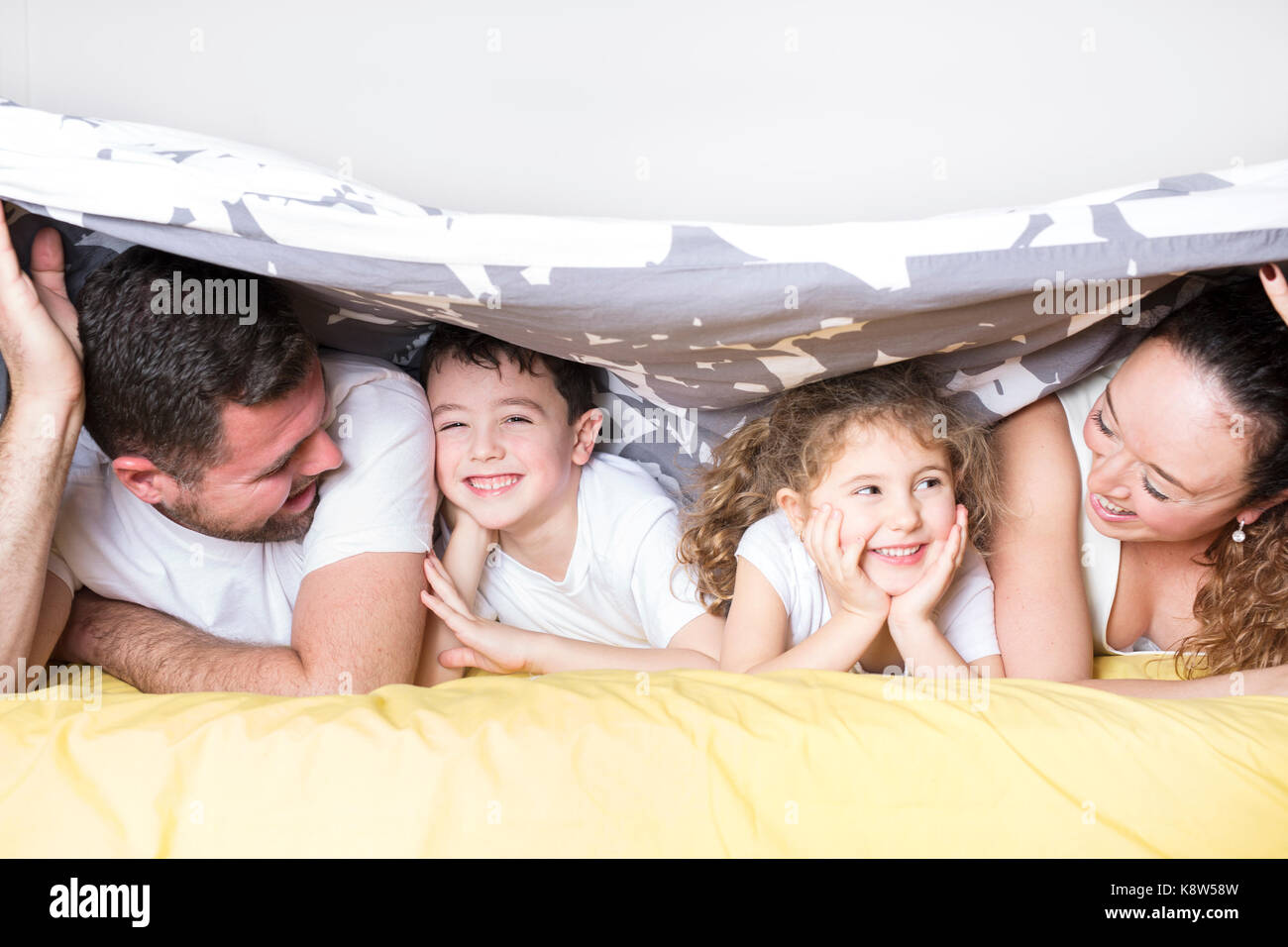family, children and home concept - happy family with two kids under blanket at home Stock Photo