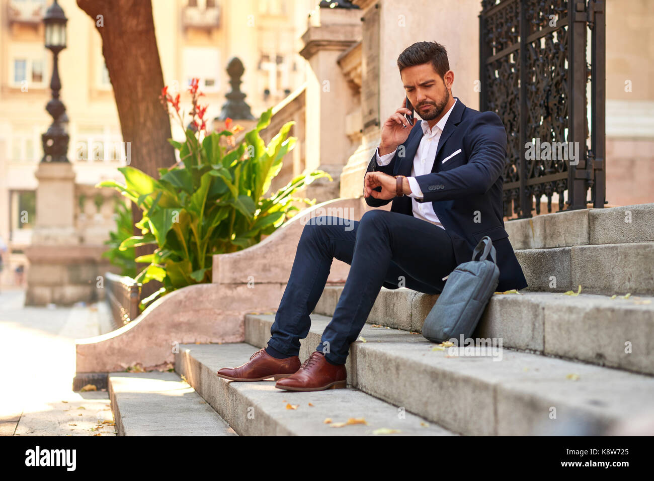 A handsome young businessman sitting on the stairs talking on his ...
