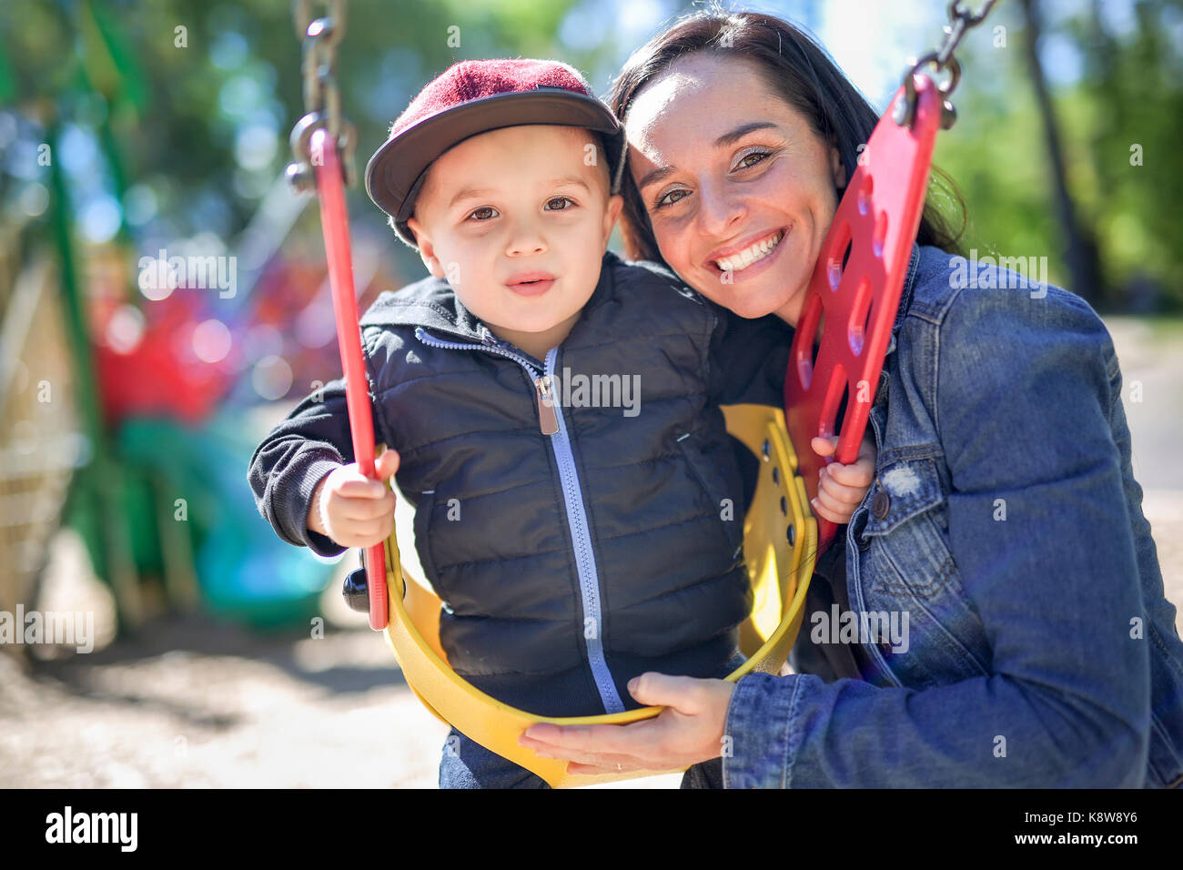 happy mother pushing son on swing in a park Stock Photo - Alamy