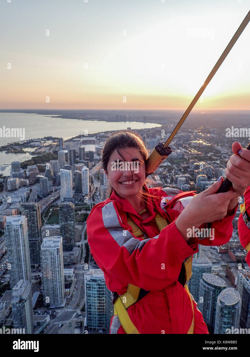 Real people doing the EdgeWalk at the CN Tower in the late afternoon. Beautiful colours of the sunset in the back Stock Photo