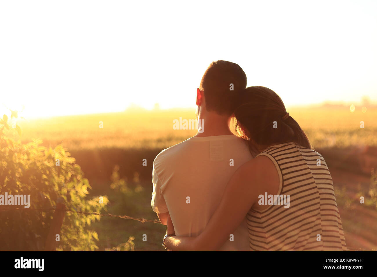 Young couple embracing and backs watching the sunset in the countryside. Love. Stock Photo