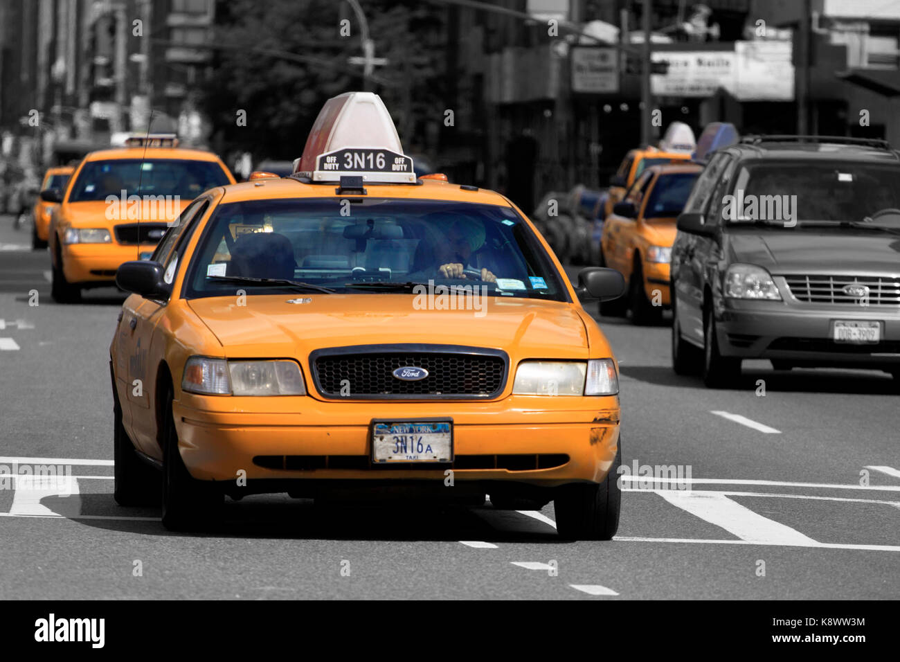 Yellow New York taxi cabs driving on a busy New York street. The cabs are brightly colored against a greyed out background Stock Photo