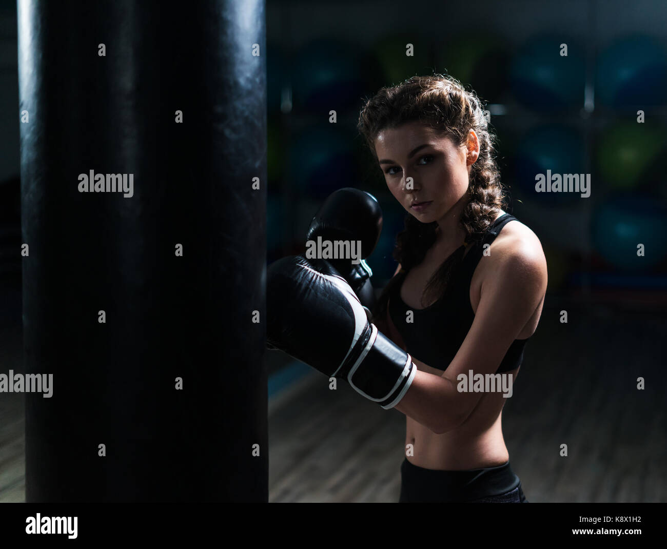 Young fighter boxer girl wearing boxing gloves in training with heavy punching  bag Stock Photo - Alamy