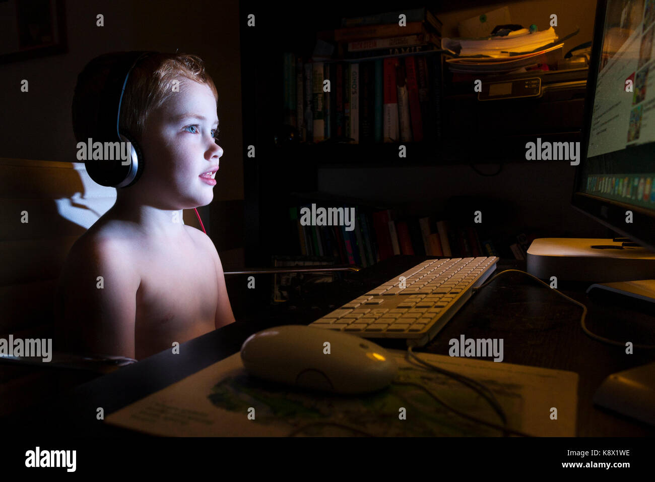 A young boy sitting at a computer watching youtube with headphones on in a dark room Stock Photo