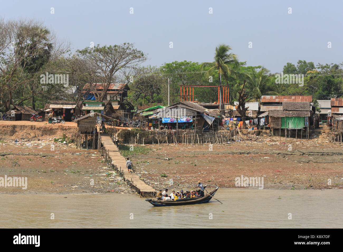 A man stands while rowing a boat loaded with passengers on the Twante Canal at a small village, Myanmar (Burma). Stock Photo