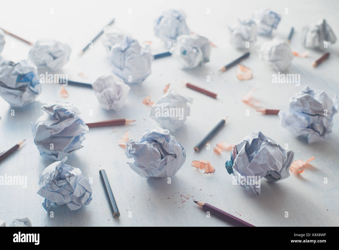 Close-up of crumpled paper balls on a white wooden background with pencils and pencil shavings. Creative writing concept. High key still life. Stock Photo