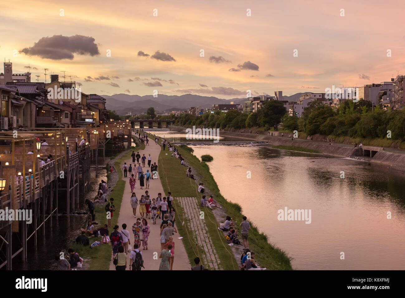 People come together along the Kamo river (Kamogawa) in Kyoto, Japan, with open air restaurants (left) during sunset. Stock Photo