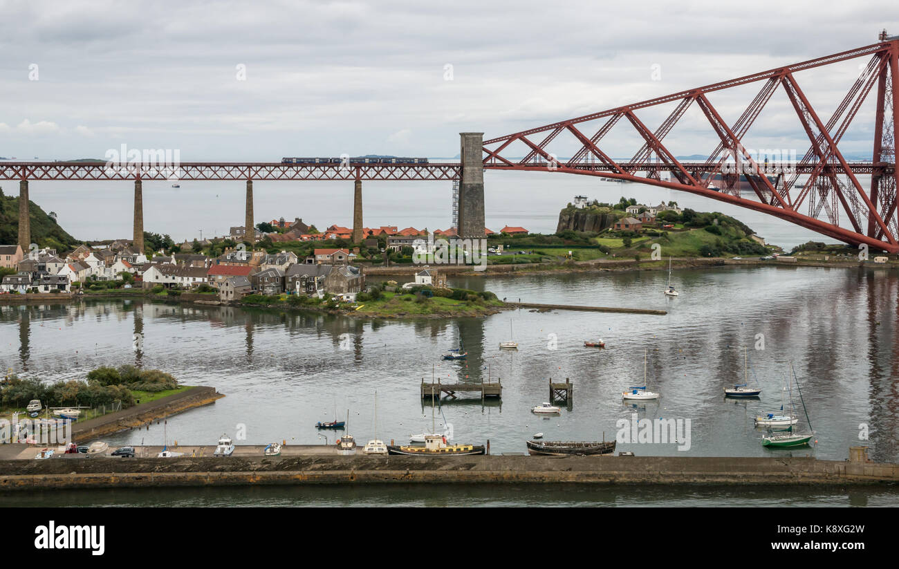 Two carriage local ScotRail train on cantilever Forth Rail Bridge over the Firth of Forth, North Queensferry, Scotland, UK, with harbour in foreground Stock Photo