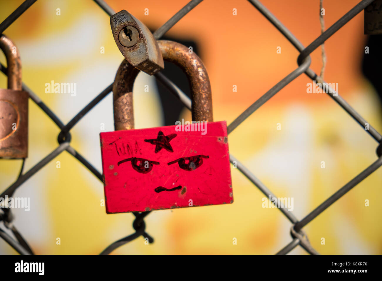 Red Padlock with Face on Chain Fence in Shoreditch East London Stock Photo
