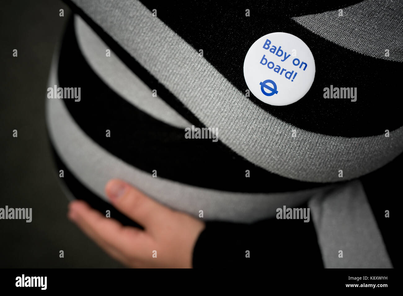 A 9-month pregnant woman holding her bump wears a London Underground Baby on Board badge before boarding the Tube (Editorial use only). Stock Photo