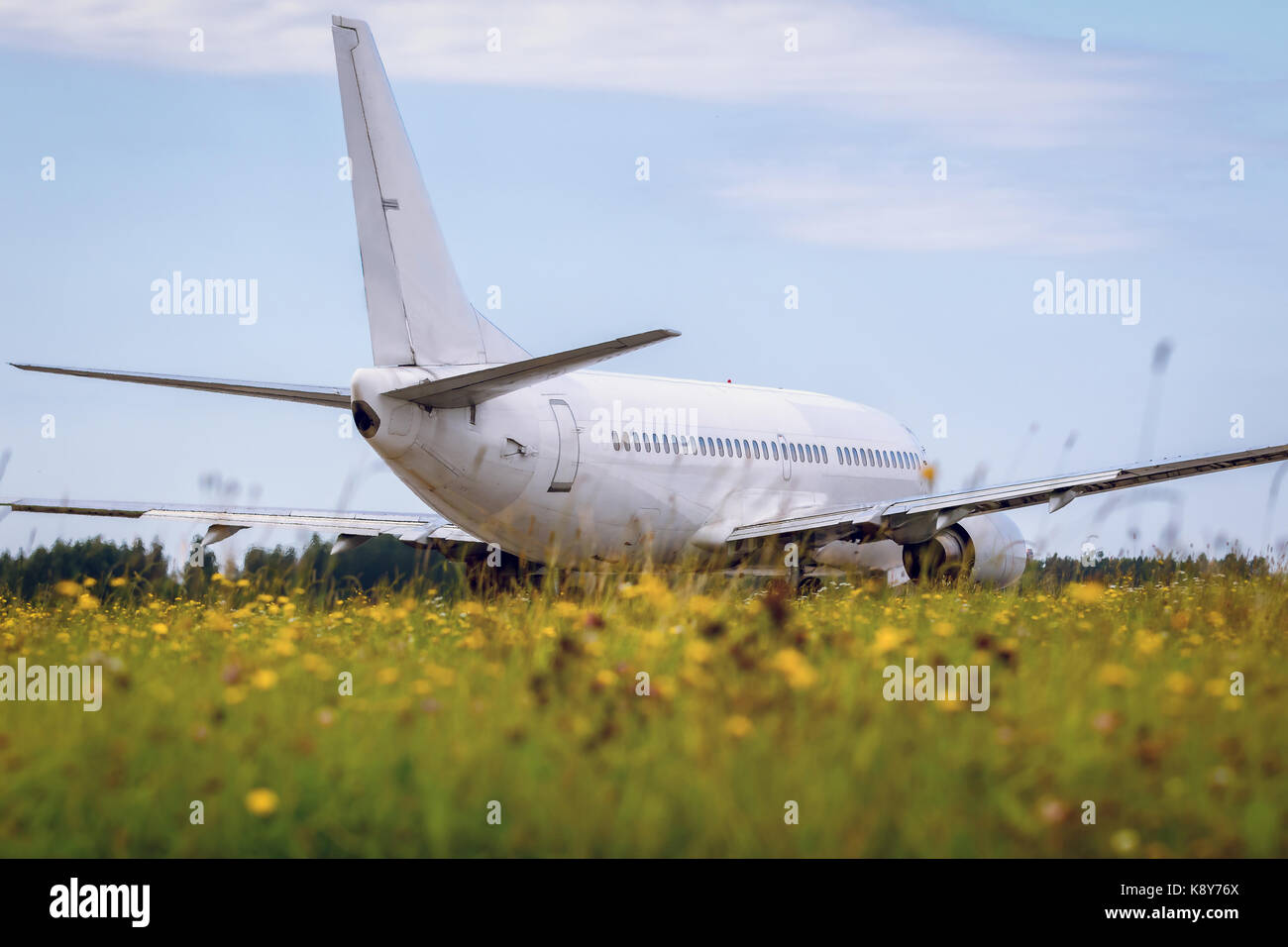 The airplane is moving on the runway against the background of the forest and blue cloud sky and in the foreground beautiful field of yellow bright fl Stock Photo