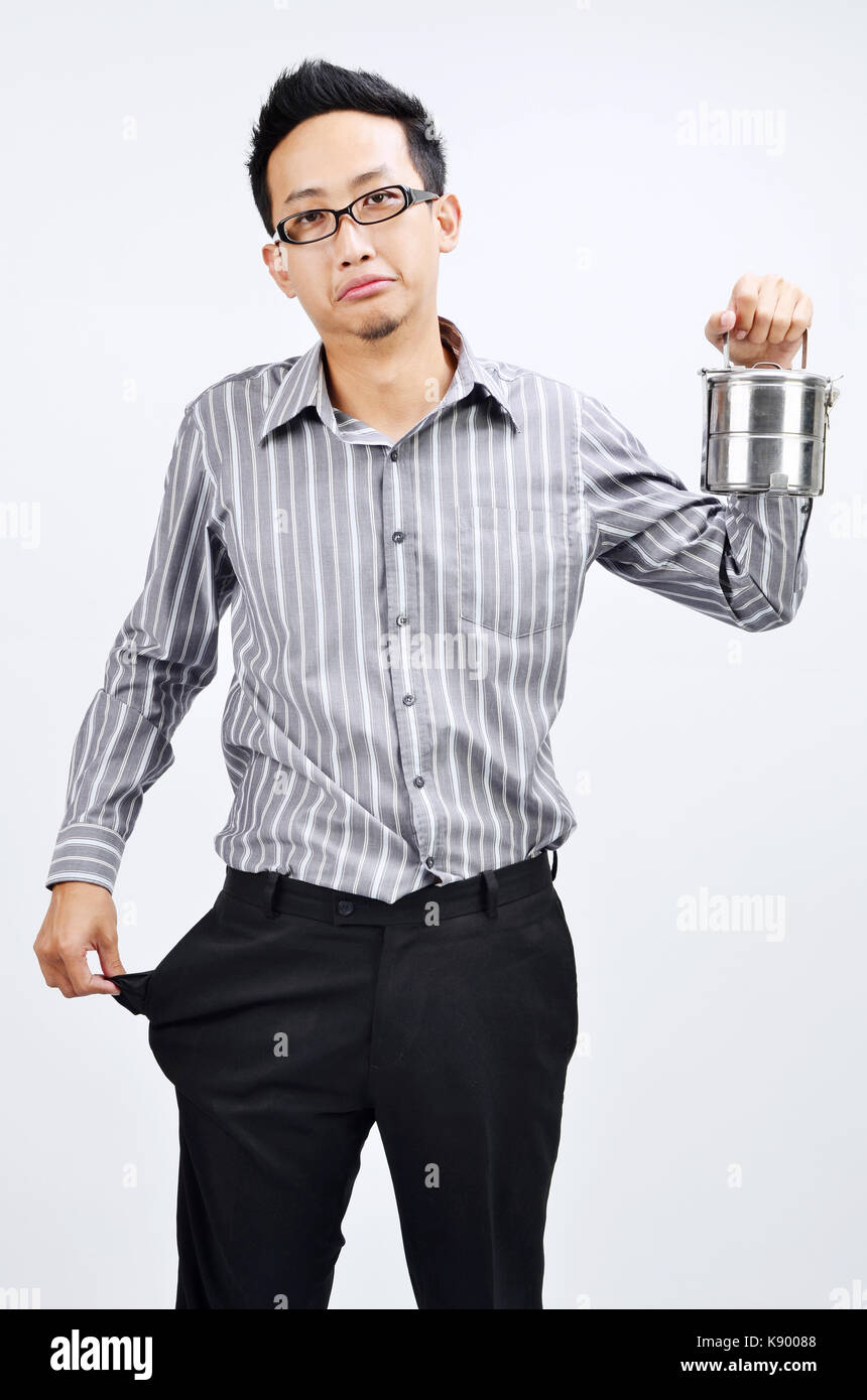 Portrait of sad Asian businessman with empty pocket, hand hold his home cook lunch box, standing isolated on plain background. Stock Photo