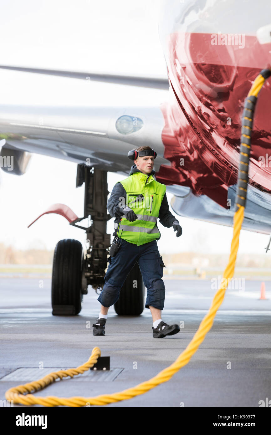 Crew Member Walking By Airplane Being Charged On Runway Stock Photo