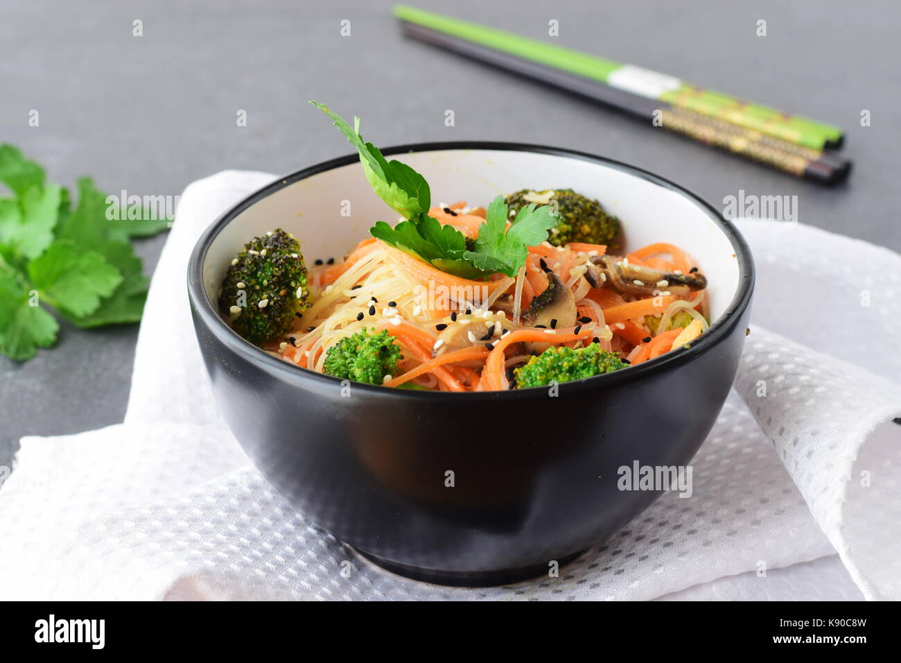 Rice noodles with carrot, broccoli and mushrooms in a black bowl on a