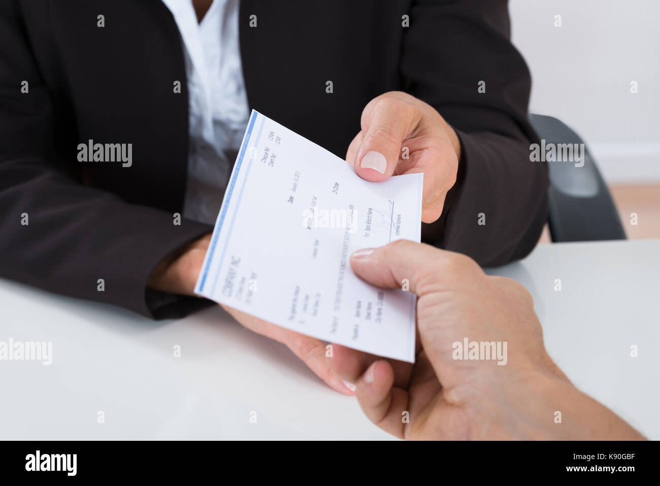 Close-up Of Businessperson Hands Giving Cheque To Other Person At Desk Stock Photo
