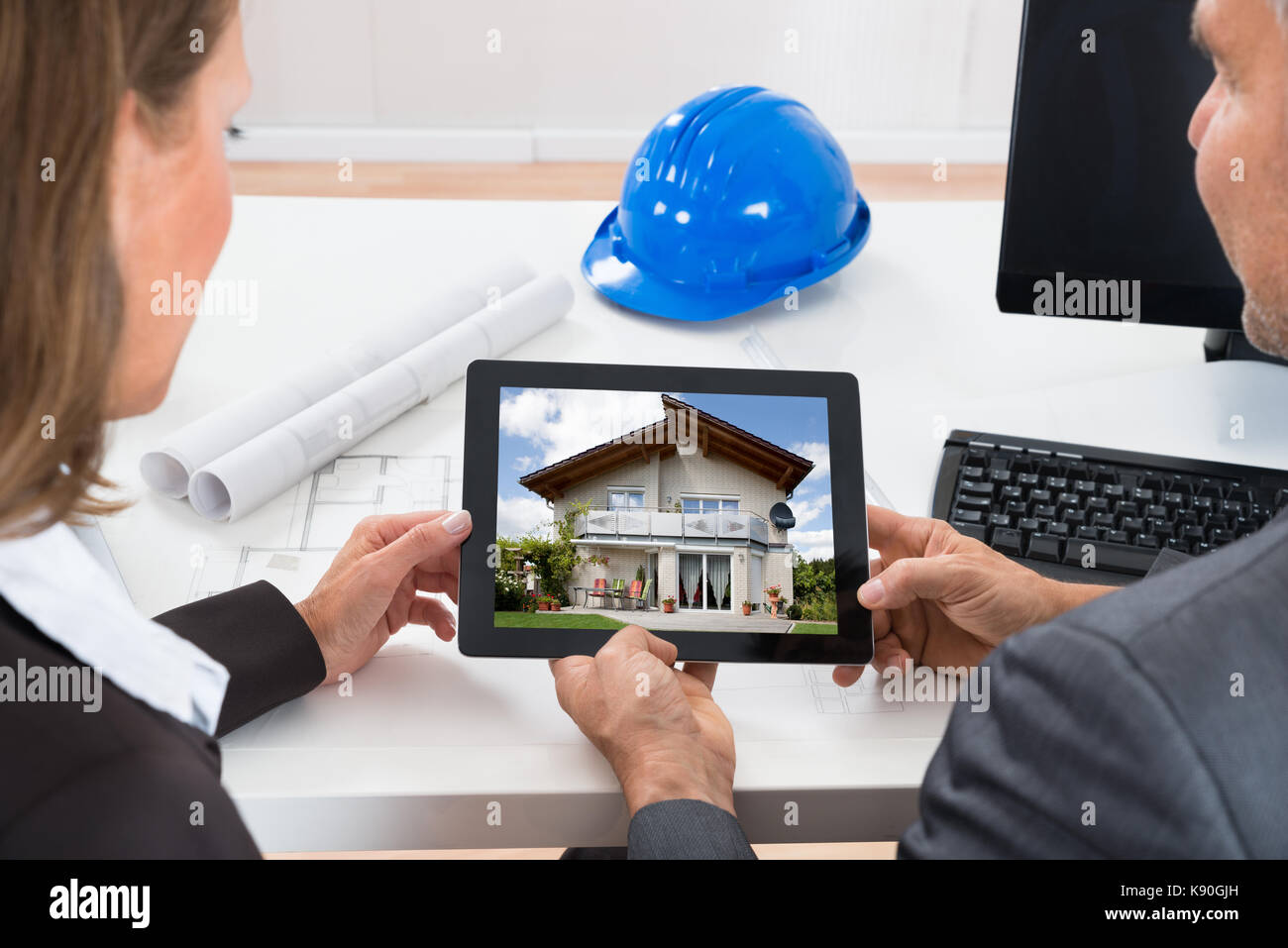Close-up Of Two Architects Looking At House On Digital Tablet At Desk Stock Photo