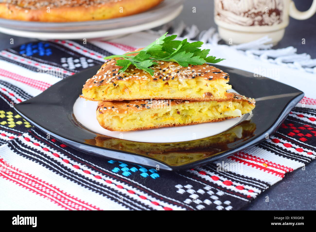 Two pieces of white cabbage pie with carrot on a black plate with cup