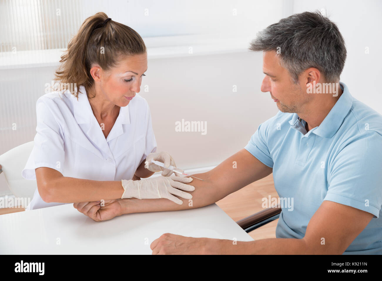 Portrait Of Doctor Drawing Blood  From Patient With Syringe In Hospital Stock Photo