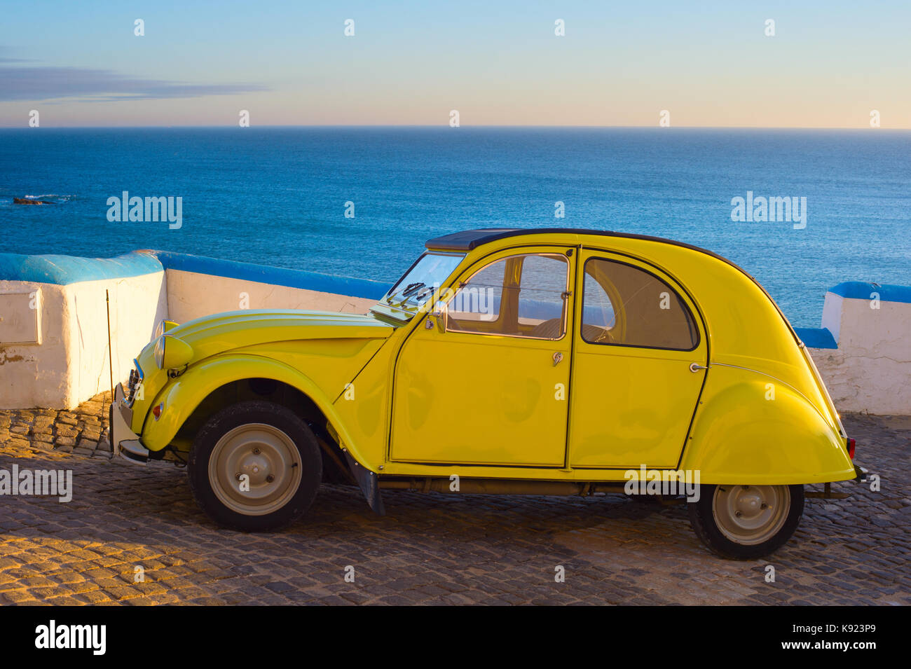 An Old yellow car in front of the ocean at sunset. Ericeira, Portugal Stock Photo