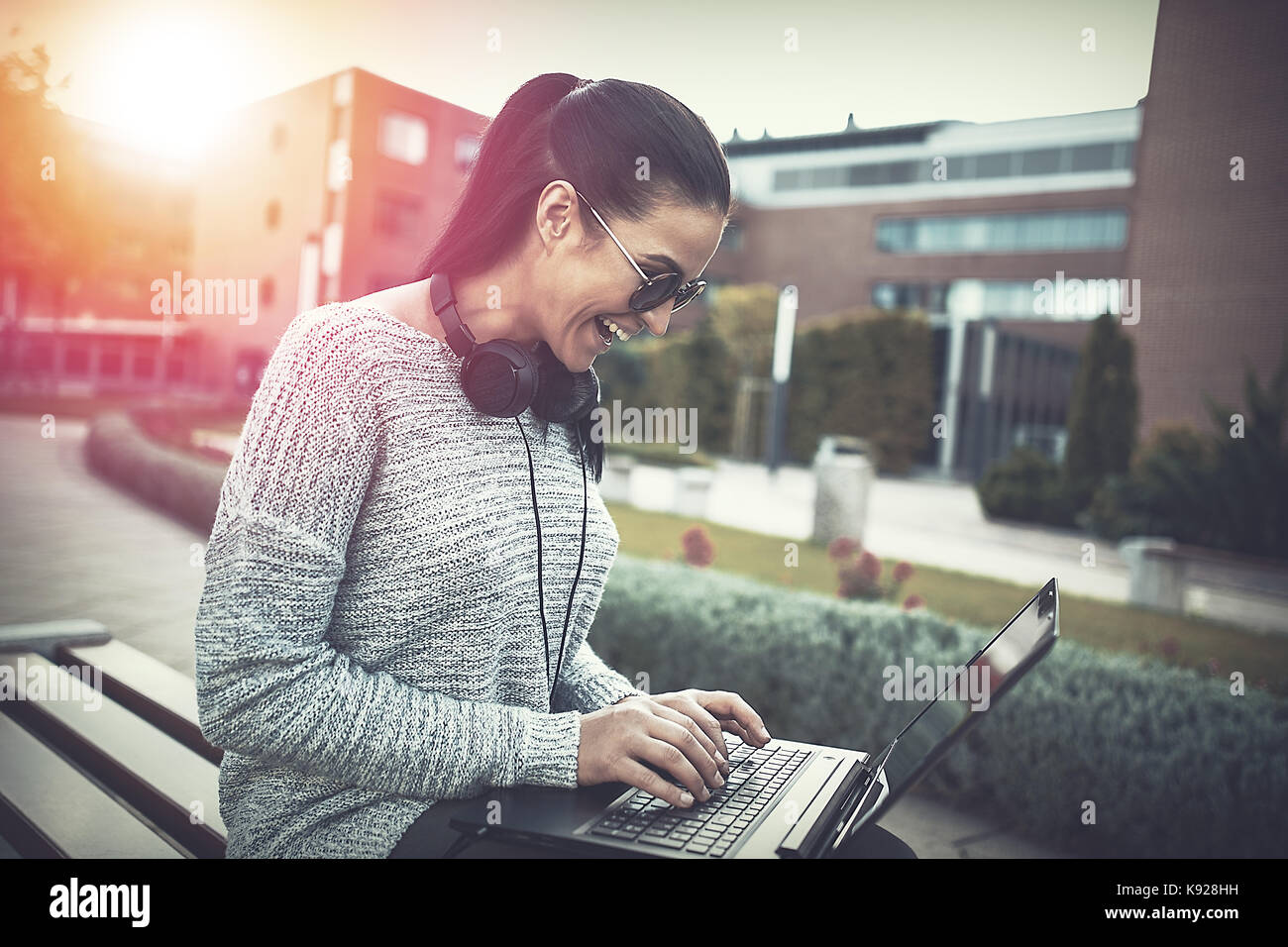 Woman laughing while typing on laptop outdoors in sunset Stock Photo