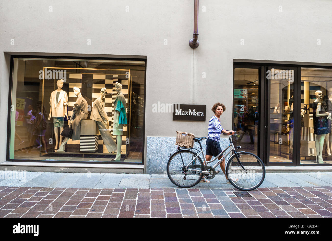 Female cyclist walking her bike in front of a MaxMara clothing shop. Stock Photo