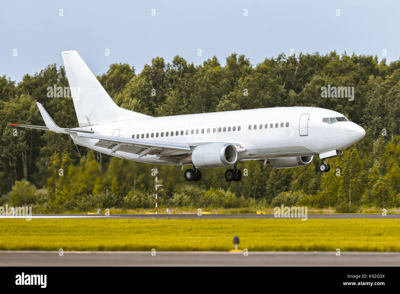 The airplane is landing on the runway at airport against the background of the forest and blue sky. Summer sunny weather Stock Photo
