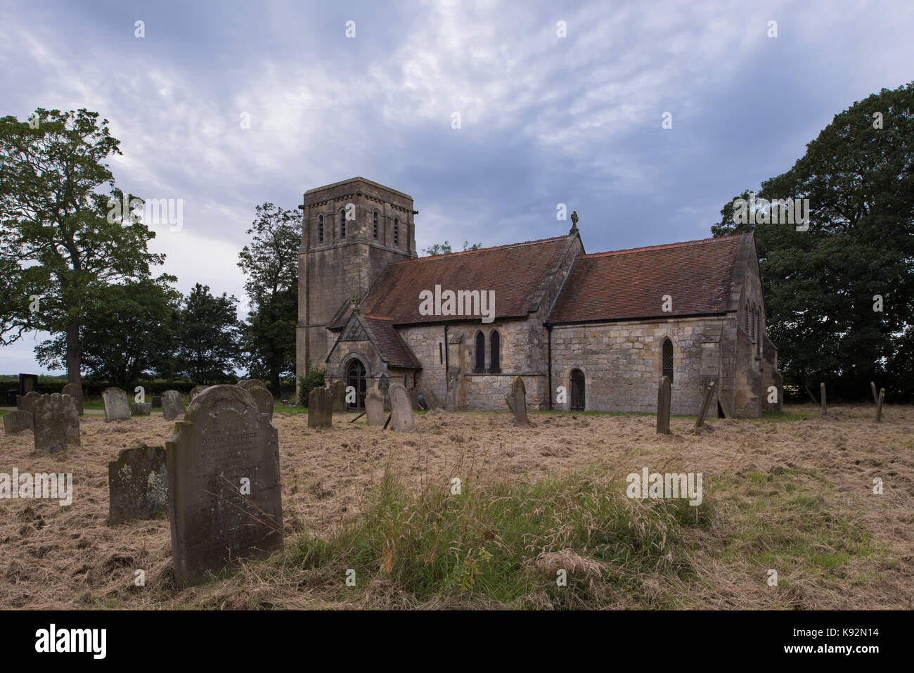 Summer evening view by headstones in the churchyard, of the exterior of historic All Saints' Church, Moor Monkton, North Yorkshire, England, UK. Stock Photo