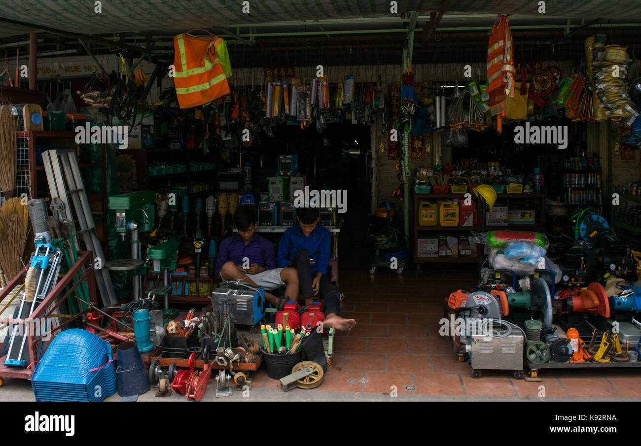 A hardware store or ironmongery shop in Phnom Penh, Cambodia. Shop is well stocked with tools on display. The shop attendants use their mobile phones. Stock Photo