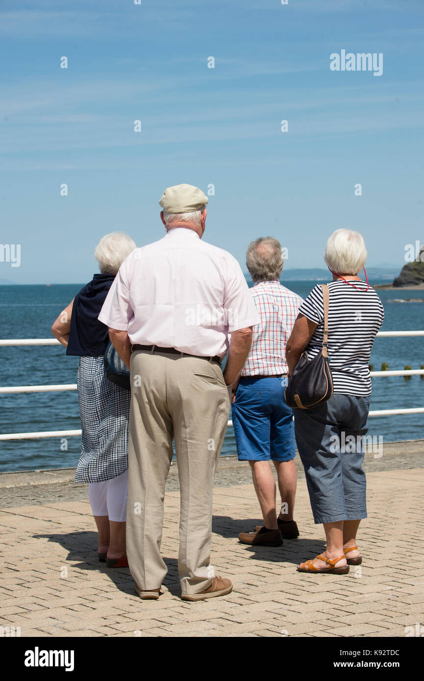A rear view of a group of 4 senior adults  enjoying a day of warm sunshine at the seaside in Aberystwyth on the west Wales coast UK Stock Photo