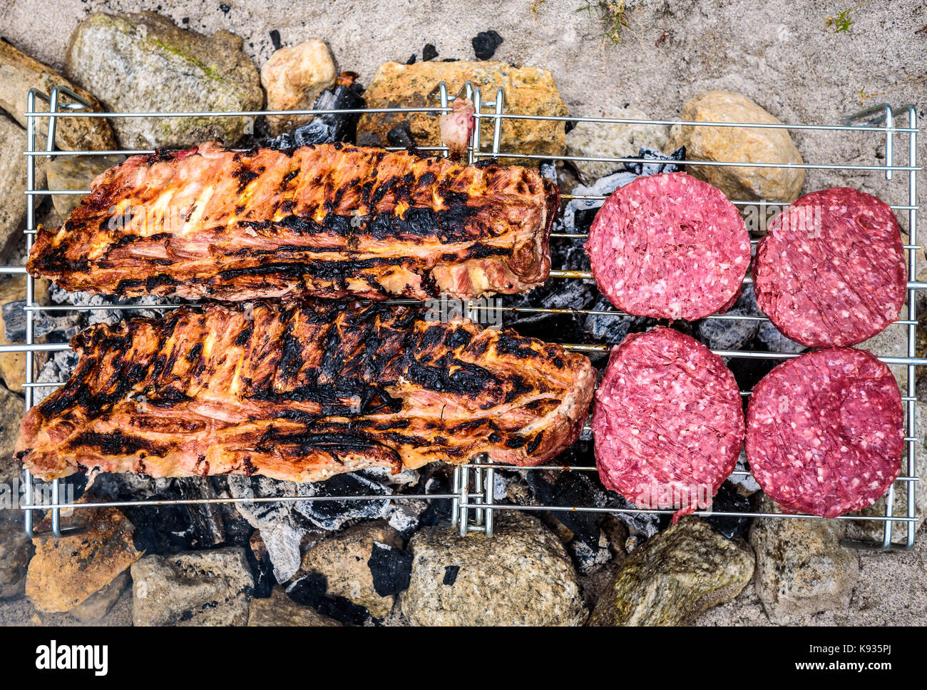Pork ribs and burgers on homemade improvised BBQ barbecue grill. Making  Churrasco and burgers on coal, fire, briquettes BBQ grill in the sand with  roc Stock Photo - Alamy